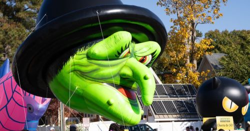 A large green balloon of a green witch's head walking in a parade.