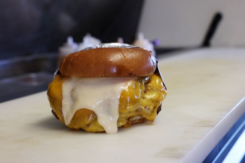 A burger with melted cheese oozing out sits on a restaurant counter