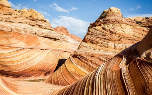 Colorful, wavy rock formations under a blue sky, showcasing intricate patterns and textures in a desert landscape.