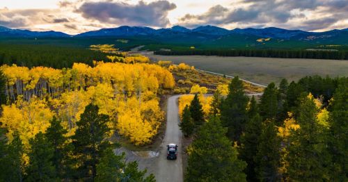 Truck driving a gravel road toward a mountain sunset, surrounded by fall color.