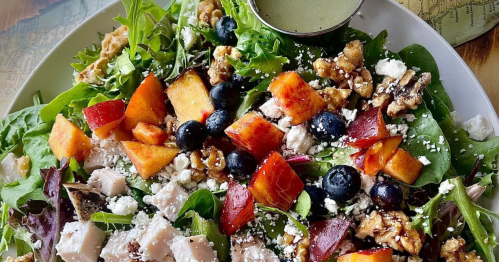 A close up image of a salad packed with fresh produce and protein. A cup of dressing sits on the side.