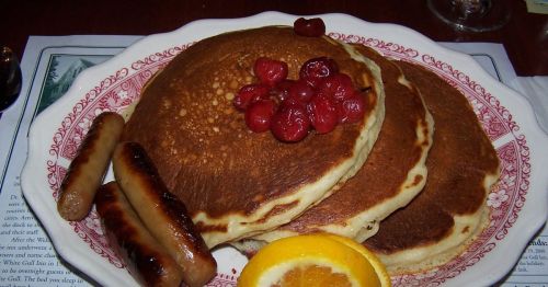 A plate of pancakes with cherries and sausage.
