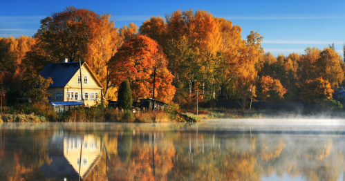 A waterfront house against fall colors with early morning fog hovering over the water.
