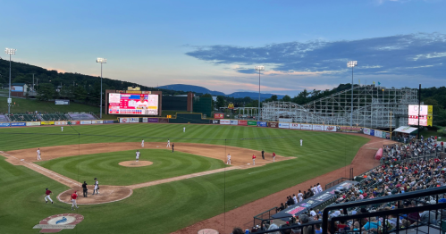 A view from the stands of the baseball field at sunset, with the amusement park roller coaster in the background.