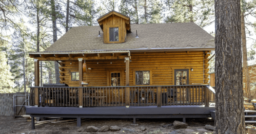 a small light-wood log cabin with a covered porch surrounnded by ponderosa pine in flagstaff arizona