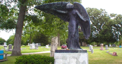 A statue of a black angel stands above a monument in a cemetery.