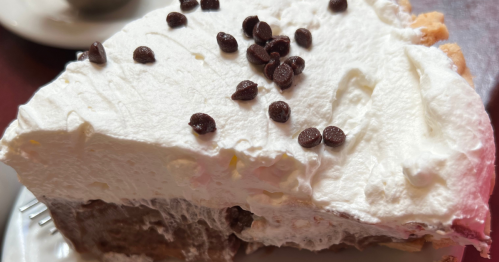 A slice of French silk pie. A thick layer of white topping on top, sprinkled with brown mini chocolate chips over a thick layer of brown chocolate pie.