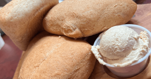 Fresh baked tan dinner rolls on a wooden serving board beside a dish of white cinnamon butter.