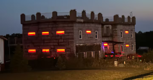 The castle exterior at dusk, featuring bright red lights illuminating the windows.
