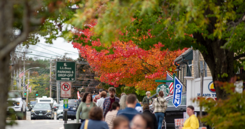 Festival goers walking down the road near vendor booths and small businesses under bright red fall foliage