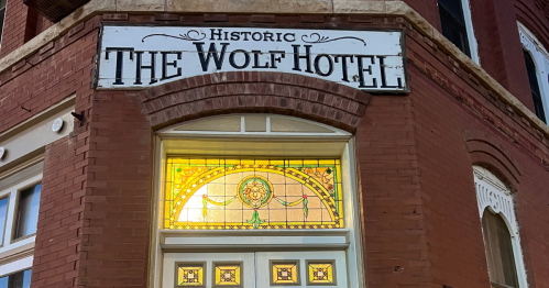 Red brick exterior with yellow and green stained glass windows around the front doors of The Wolf Hotel