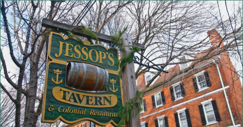 Exterior of Jessop's Tavern showing the green and yellow sign with a historic barrel in front of a colonial-style brick building.