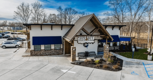 Exterior of River Town Grill, a modern, craftsman building painted white and blue with bare trees in the background.