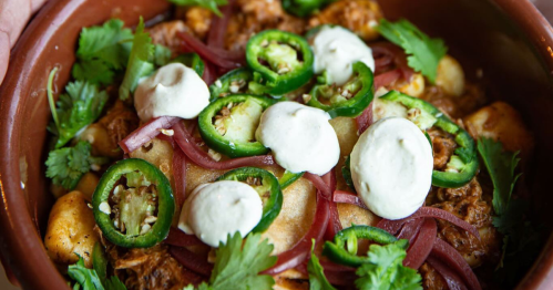 A rich gnocchi dish topped with meat, pickled red onions, jalapeños, and a creamy sauce.