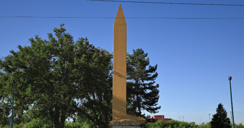 A giant golden spike statue surrounded by green trees on the left side.