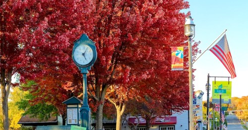 A green clock bearing the words "Green Lake" stands before a tree with red fall foliage.