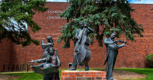 Five statues of musicians performing with a red brick wall behind them.