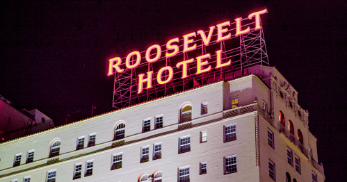 exterior of the roosevelt hotel, a famous and infamous hotel in downtown los angeles with its iconic rooftop sign aglow in neon lights against a night sky