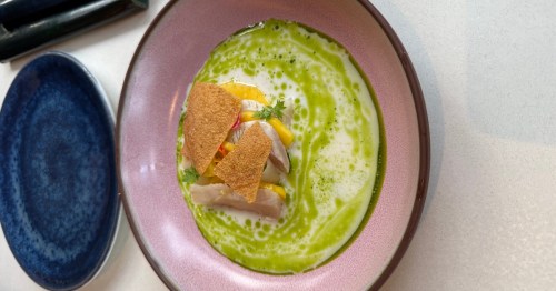 Food prepared in a fine-dining style with a green soup and crumbles above.