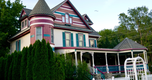 An old pink and white home with a white pergola in front in Lindsborg