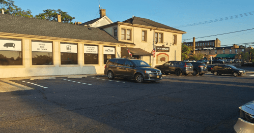 The exterior of Local Smoke, an elongated barbecue restaurant, in a parking lot in early evening.