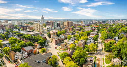 A bird's eye view of Madison with buildings, strees, green trees, and a blue sky