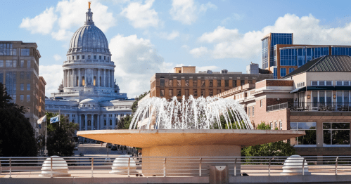 A circular fountain spraying water into the center with the white Wisconsin State Capitol in the background