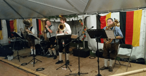 members of a german band, all dressed in leiderhosen, perform on stage with german flags in the background at the annual oktoberfest in fredericksburg, texas