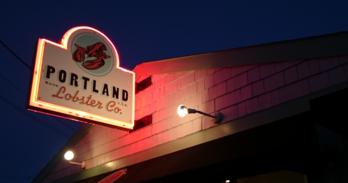 A sign reading "Portland Lobster Company" illuminared by street lights.