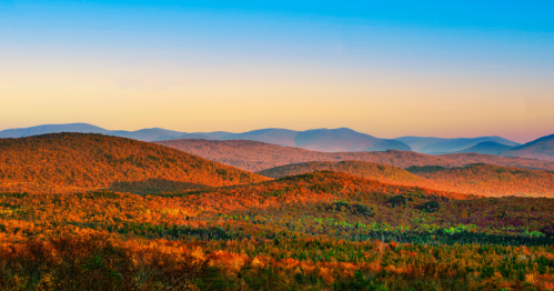 Green mountains covered in vibrant fall foliage under a bright blue sky in Vermont