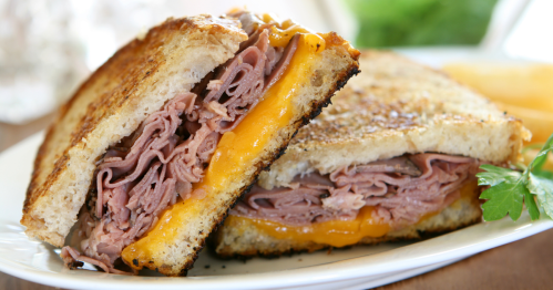 A toasted sandwich filled with thinly sliced roast beef and melted cheddar cheese, cut in half and served on a plate.