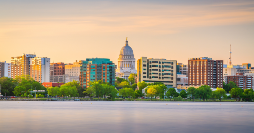 A pink sunset behind the Madison with the capital building in the middle and Lake Monona in the foreground