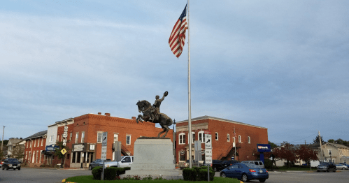 A statue of a man on horseback in the center of a traffic circle in a small town.