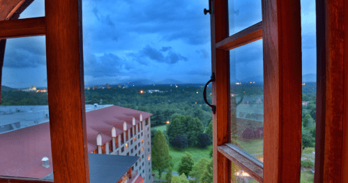 View through wooden window of Omni Grove Park Inn, with red brick roof and mountains beyond under an omnious, cloudy sky
