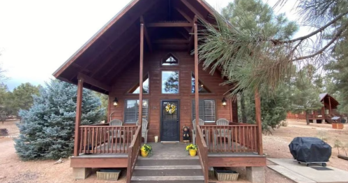a charming cabin with a covered porch featuring seating and yellow decorative accents on a property with at least one other cabin and pine trees in overgaard, arizona