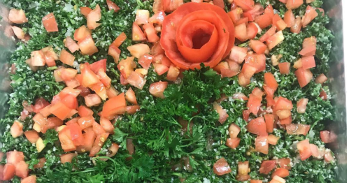 A close-up of tabbouleh salad with chopped parsley and tomatoes arranged in a rose shape.
