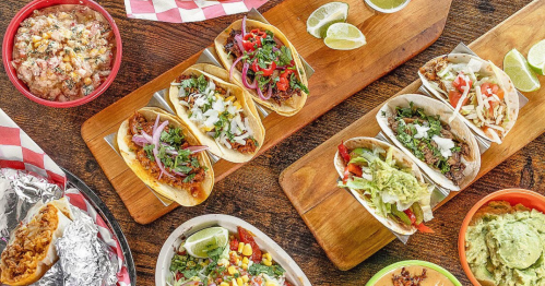An overhead view of a table covered with a variety of tacos, dips, and bowls of food.