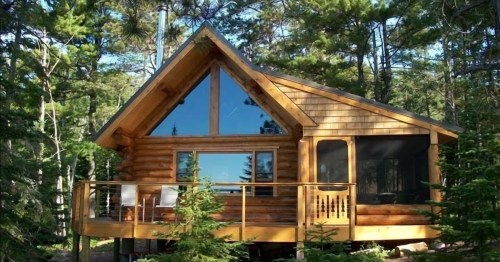 A log cabin with large windows reflecting the sky is nestled among the pine trees on a Minnesota ridge.
