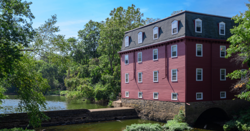 Bright red mill on the river set against green foliage under a blue sky