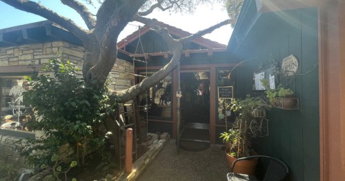A restaurant with a cut-wood exterior called 'Treehouse Cafe' sits amid trees and other plants.
