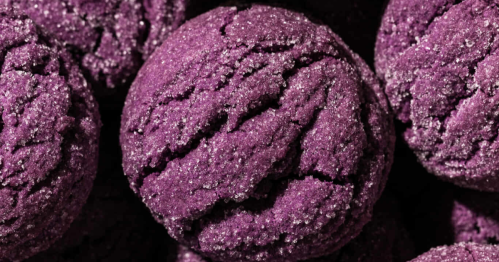 A close-up of a deep purple, crinkle-top cookie generously dusted with sparkling sugar crystals.