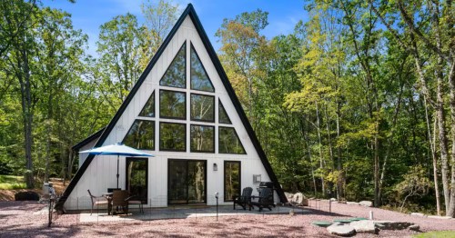 Striking white and wood A-frame with a large glass front and outdoor seating area on a sunny day.