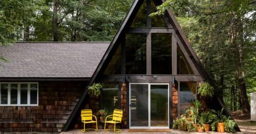Rustic, dark wood A-frame cabin with a porch, nestled among the tall, dense trees near Greentown, PA.