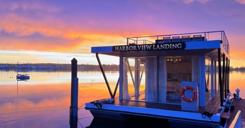 The Patriot at Harbor View Landing, a modern floating home, at sunset with a striking sky reflecting on the water.
