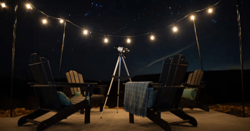 Adirondack chairs and a telescope beneath string lights and a constellation-filled night sky.