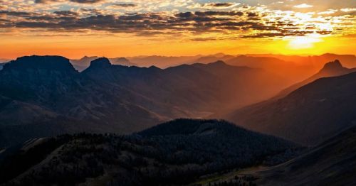 A vibrant and dramatic gold and red sunset over layers of mountains.