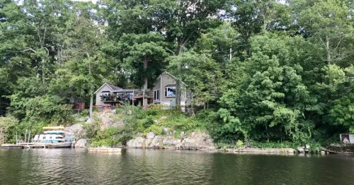 A two-story lakeside cabin surrounded by a canopy of trees.