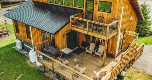 The exterior of a two-level cabin with a wood exterior and a large porch.