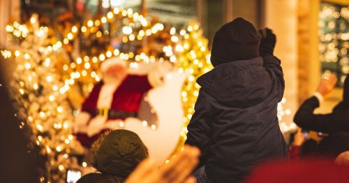 A crowd of people watching a Christmas parade with a child waving at Santa on a float.