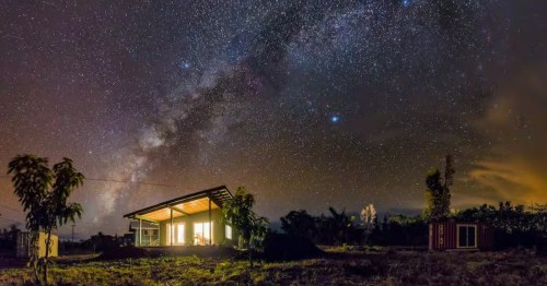 A vacation rental in Hawaii is lit up at night as bright stars shine overhead.